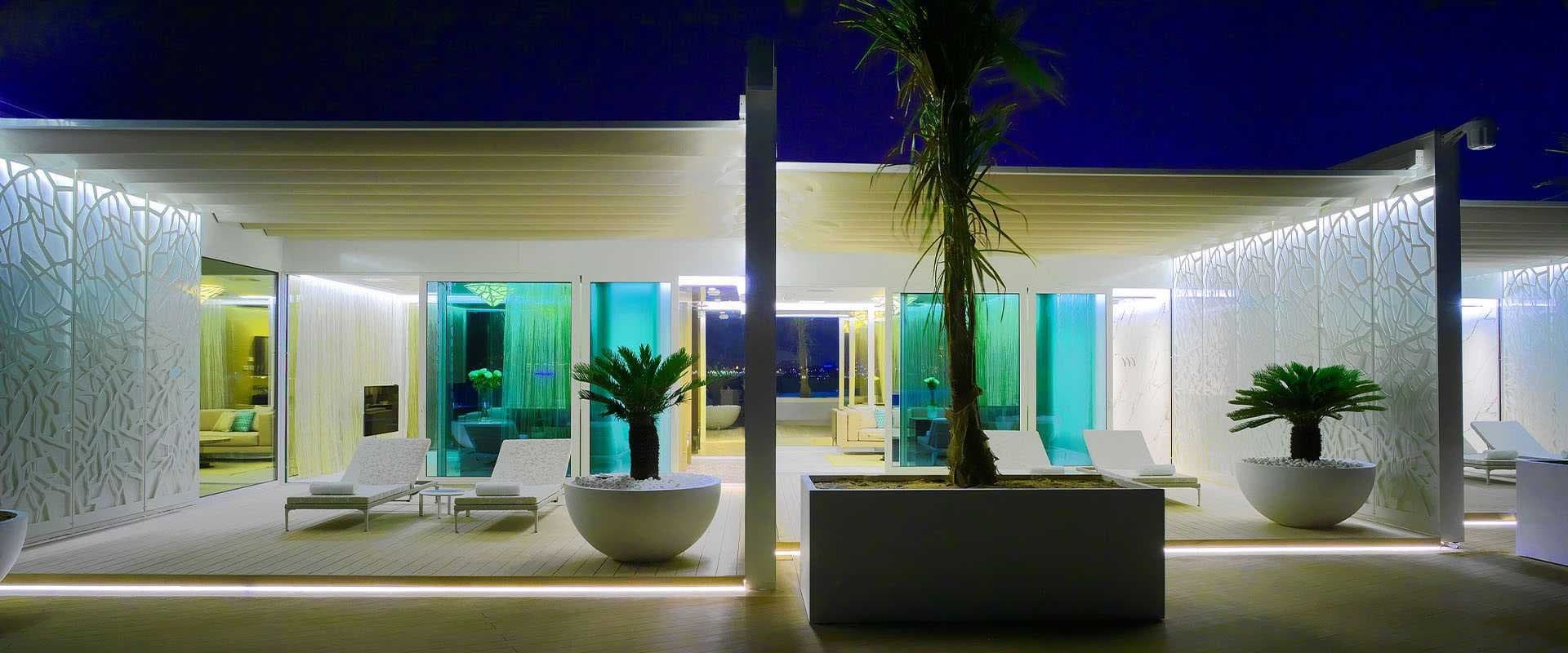 Terraza de hotel con pérgolas y persianas correderas iluminadas en azul y verde al atardecer