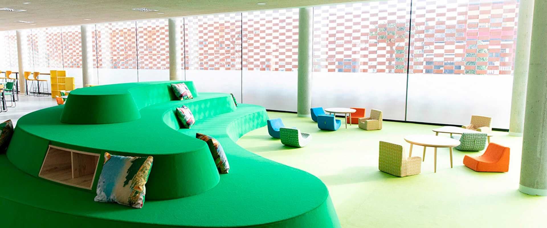 Espacio público interior con asientos curvos verdes y mobiliario infantil de colores