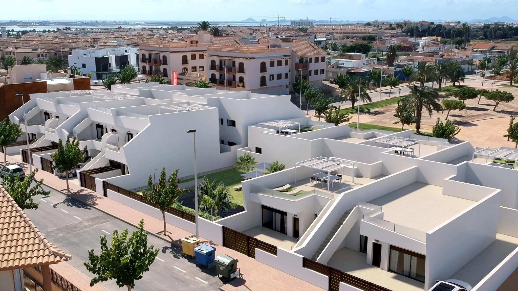 Vista aérea de un conjunto residencial de viviendas blancas con terrazas y pérgolas junto a una calle arbolada