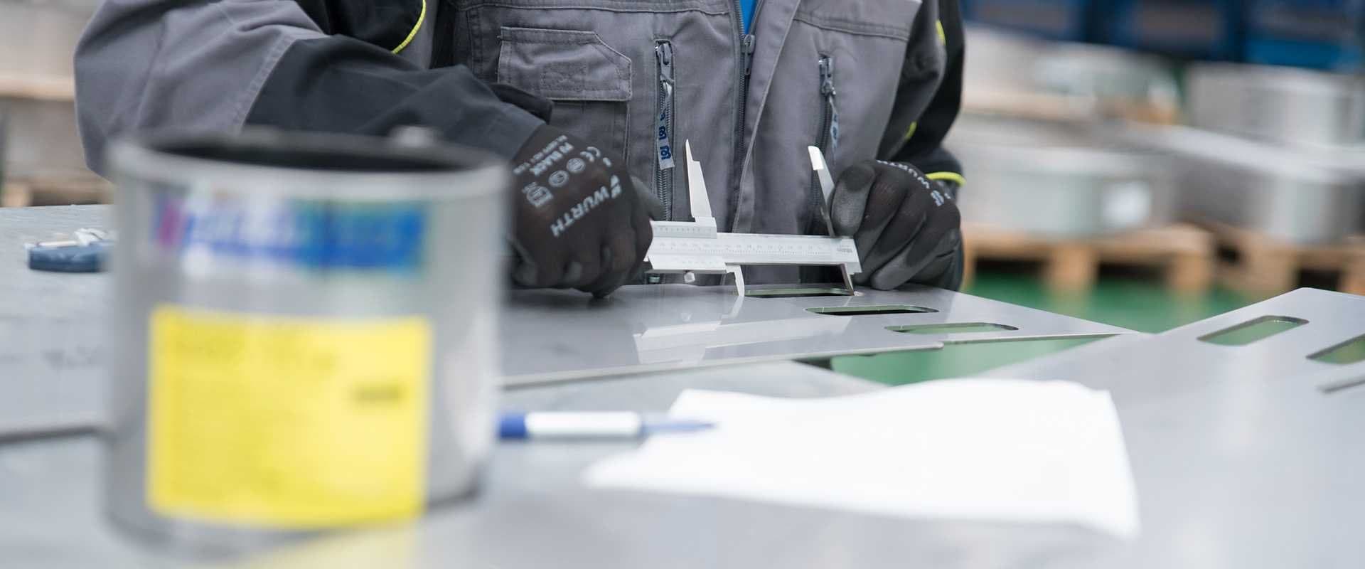 Manos sosteniendo un calibre de medición sobre una abrazadera metálica junto a un bote de pintura