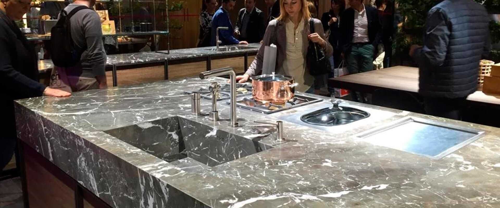 Encimera de cocina de mármol expuesta en una feria comercial con visitantes alrededor