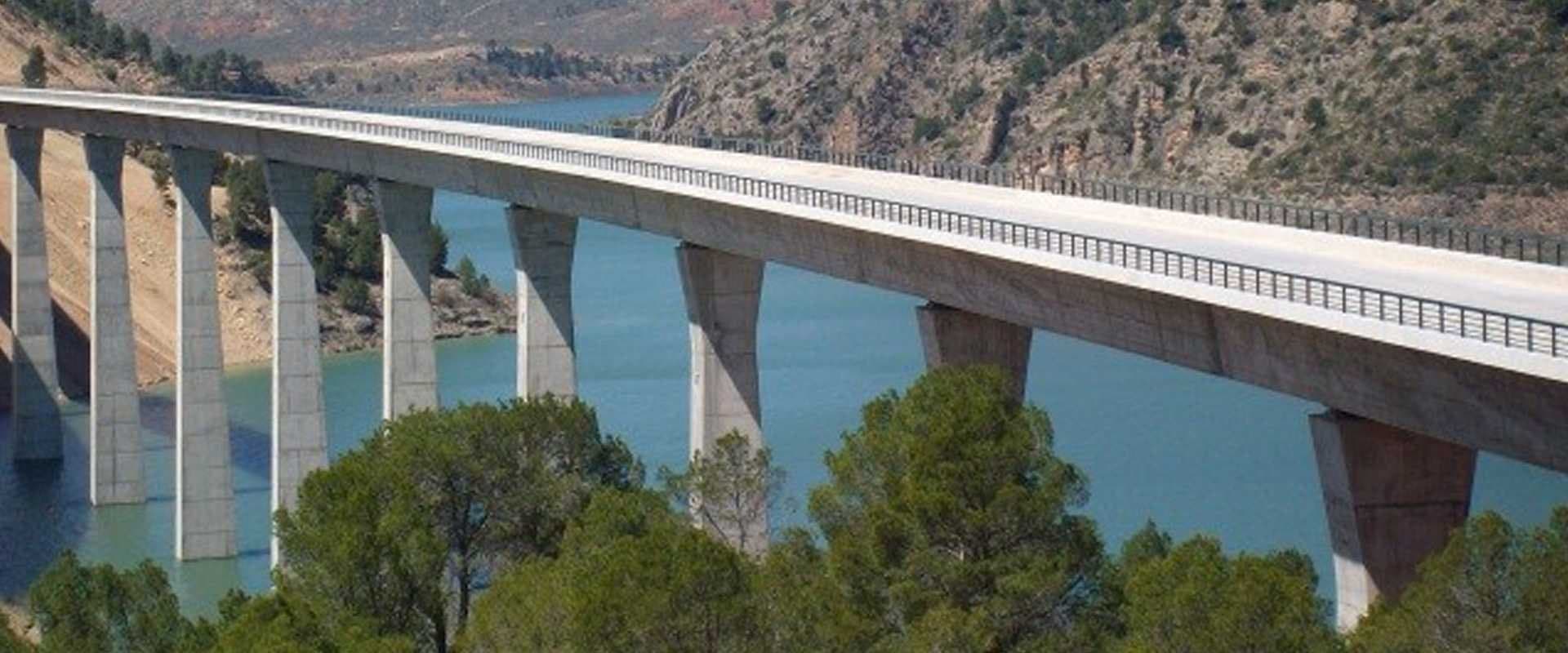 Viaducto de hormigón sobre un embalse rodeado de montañas y pinos