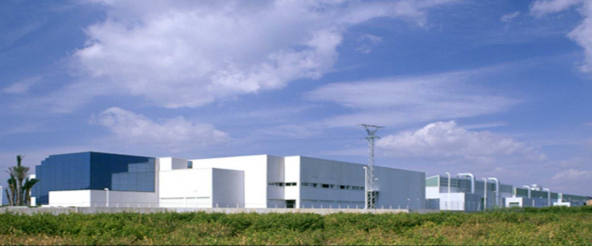 Conjunto de naves industriales blancas bajo un cielo azul con nubes