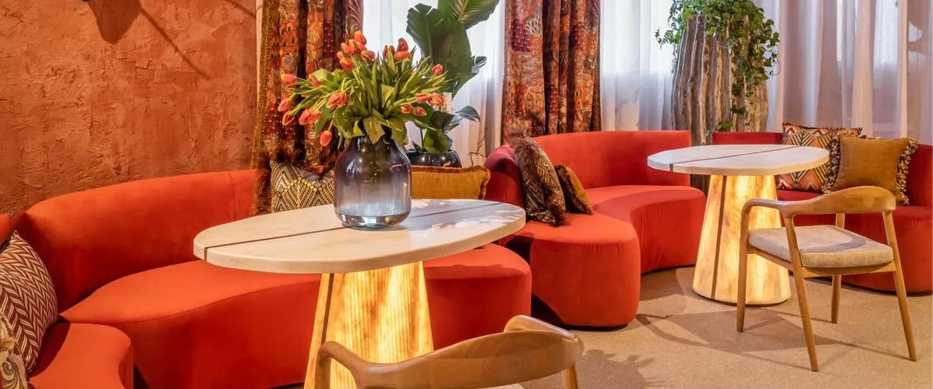Salón con sofás curvos en terracota, cortinas estampadas y un jarrón con tulipanes