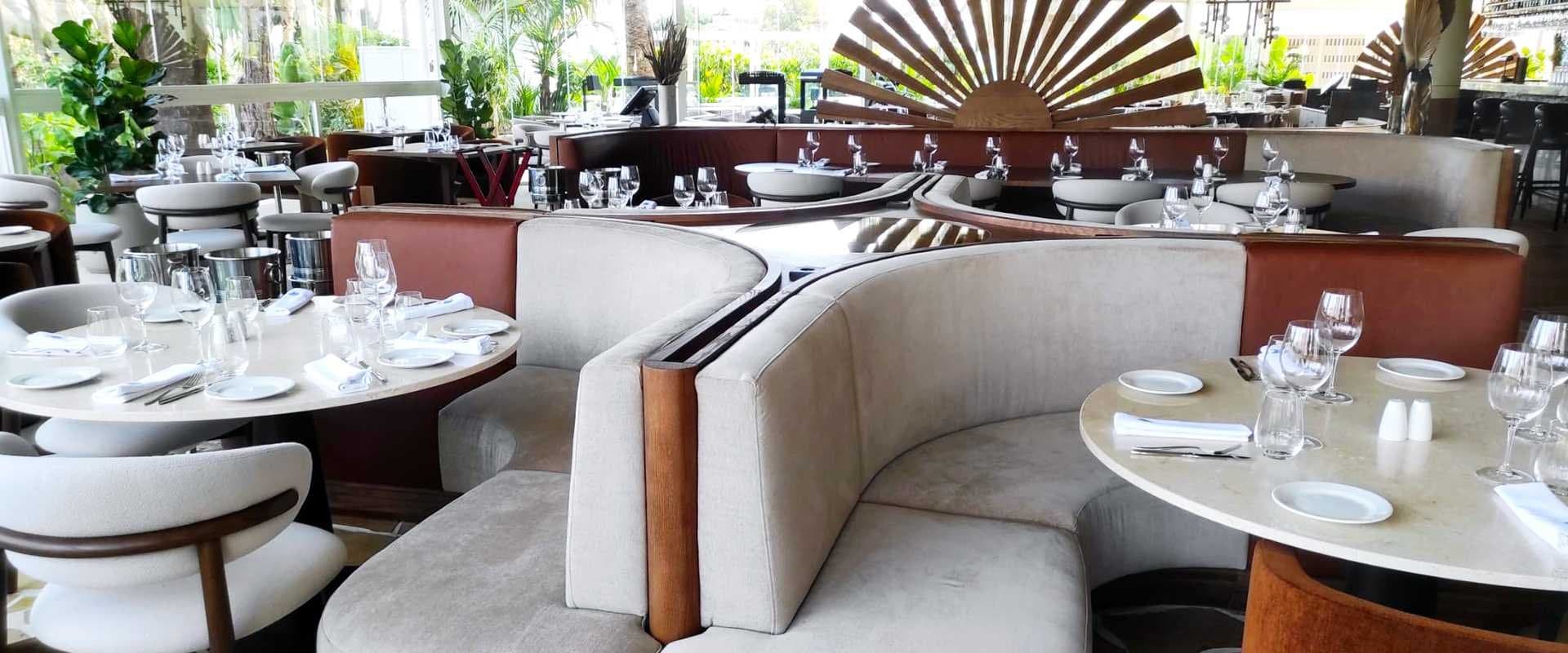 Terraza de restaurante con mampara de madera en forma de abanico y bancos tapizados en crudo