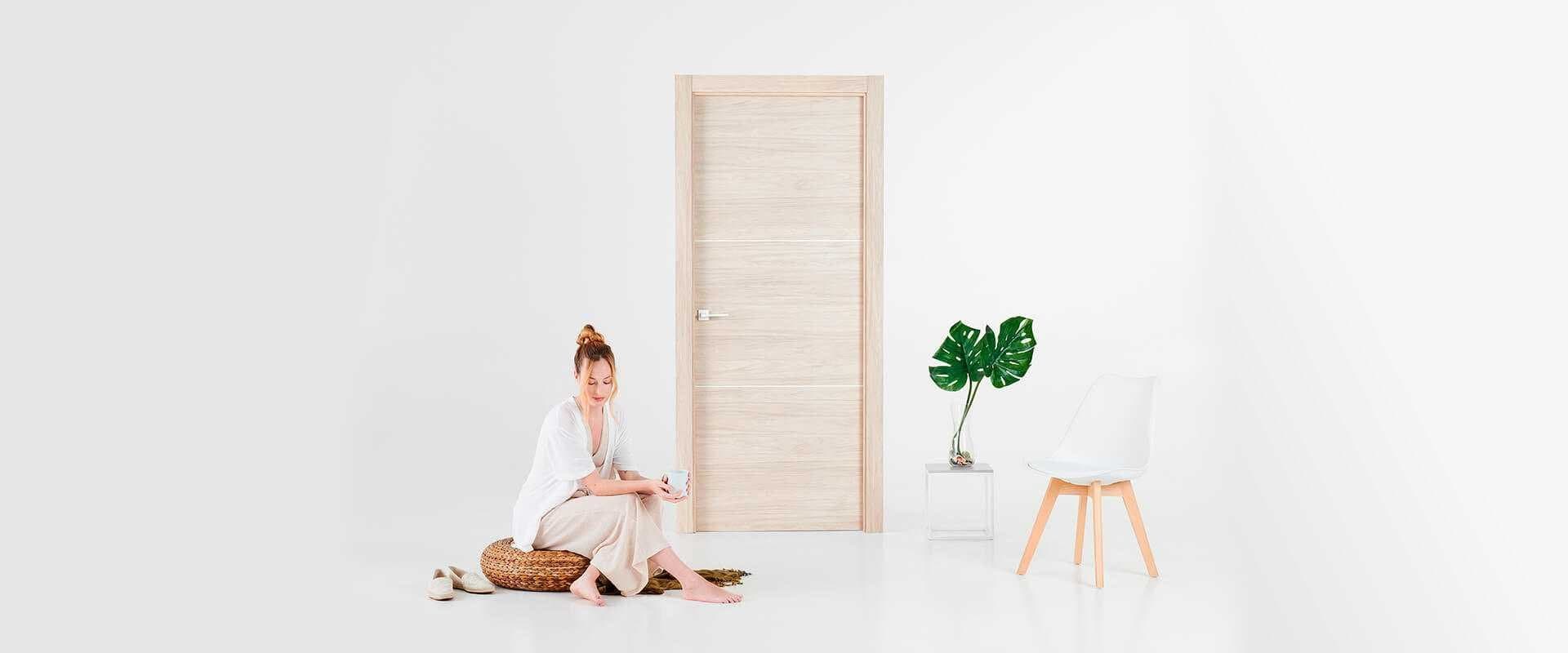 Puerta interior de madera clara junto a una mujer sentada y una silla blanca