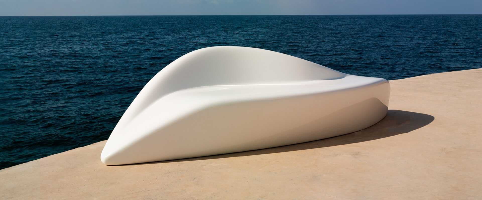 Banco urbano escultórico de color blanco sobre un paseo marítimo junto al mar