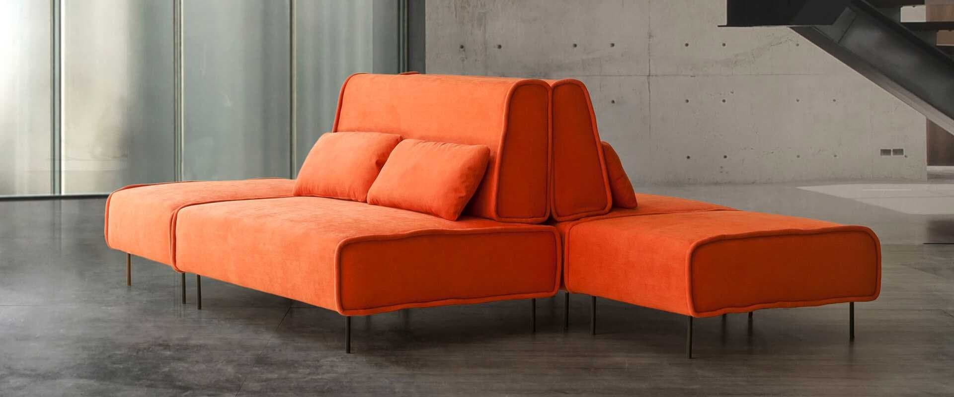 Sofá modular tapizado en naranja con cojines en un loft de paredes de hormigón