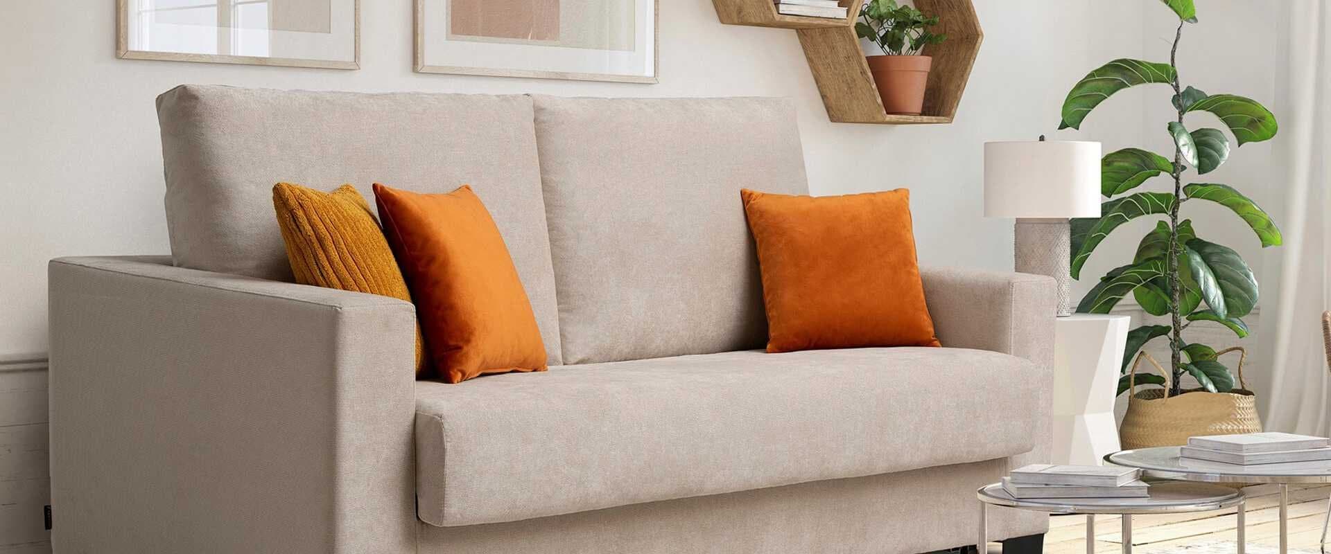 Sofá tapizado en beige con cojines naranja y mostaza junto a una planta