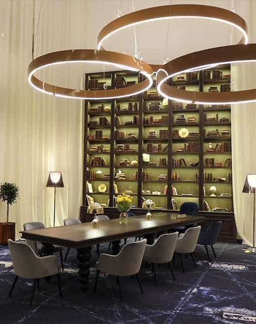 Sala de reuniones con mesa larga, sillería y estantería de biblioteca iluminada