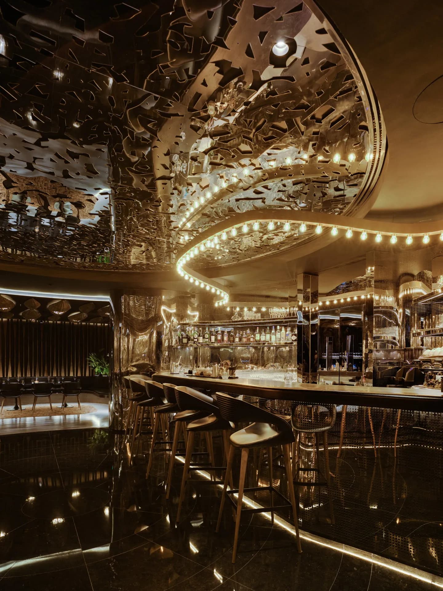 Bar de restaurante con techo escultórico metálico, guirnalda de luces y taburetes de madera