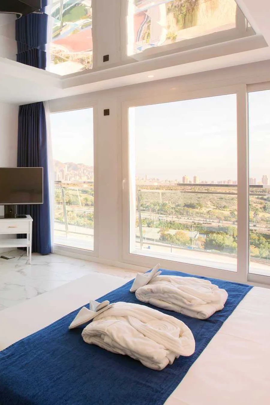 Habitación de hotel con cama, televisión y ventanal panorámico con vistas a la ciudad