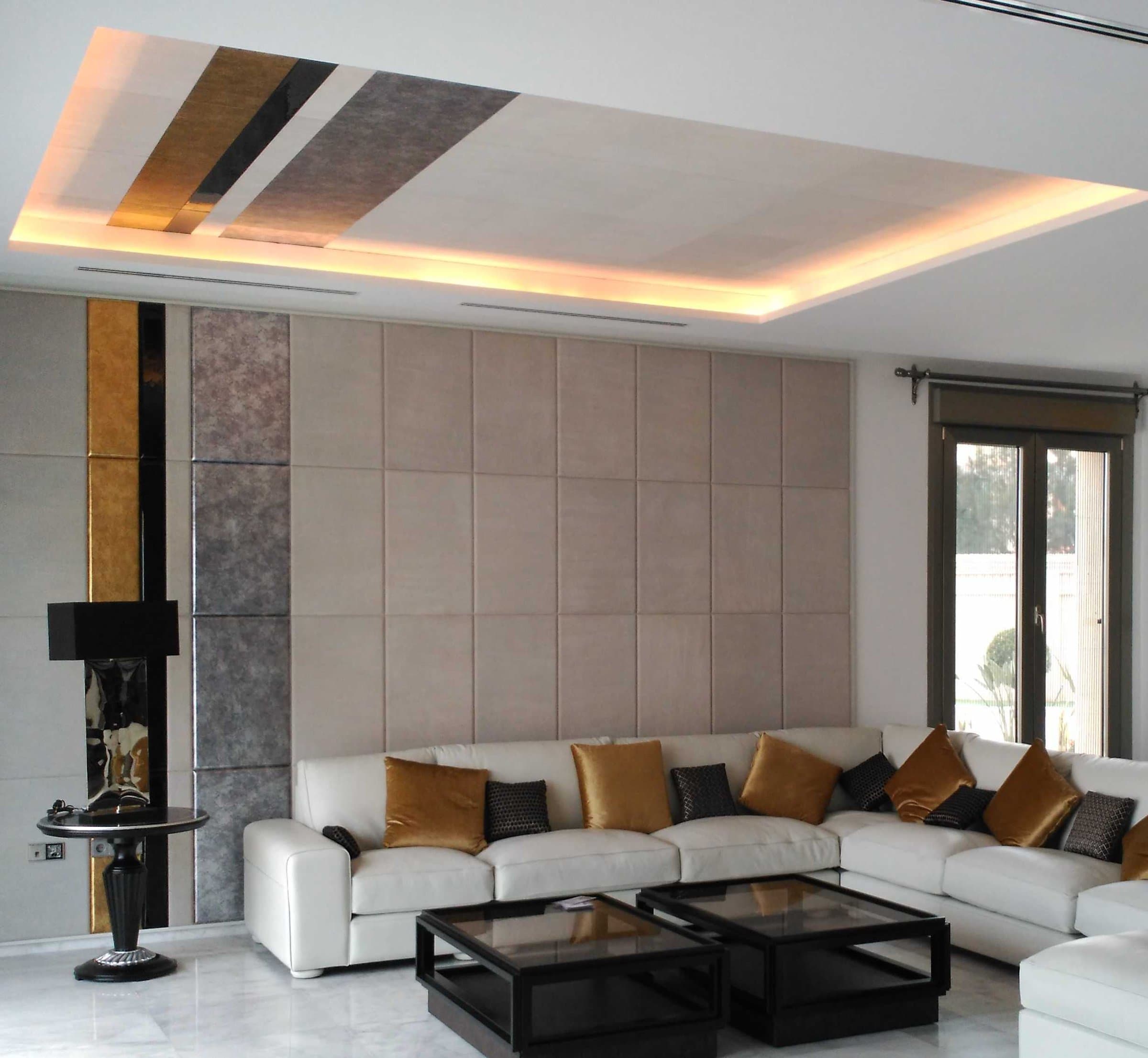 Salón con sofá blanco, cojines dorados y techo con iluminación indirecta