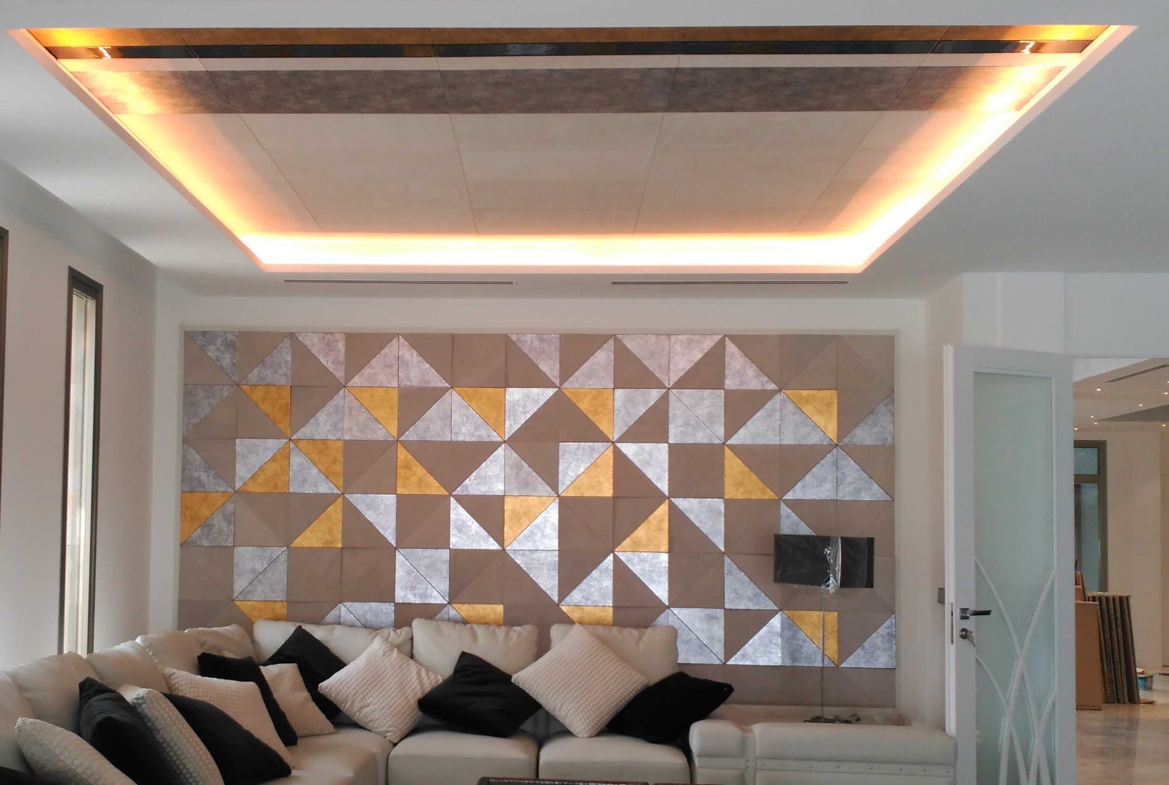 Salón con panel de pared geométrico en tonos dorados y plateados y techo con iluminación indirecta