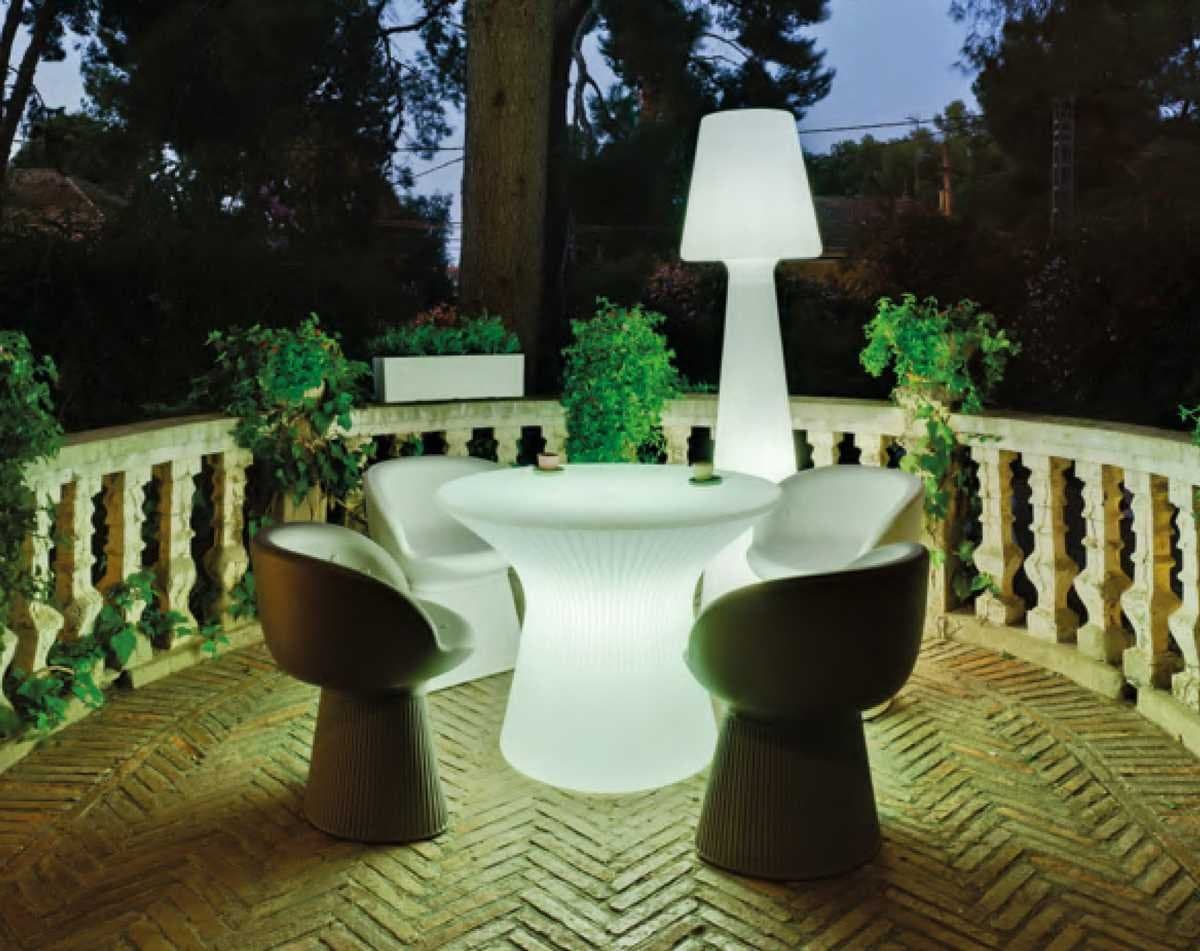 Mesa y sillas de exterior iluminadas en una terraza nocturna rodeada de vegetación