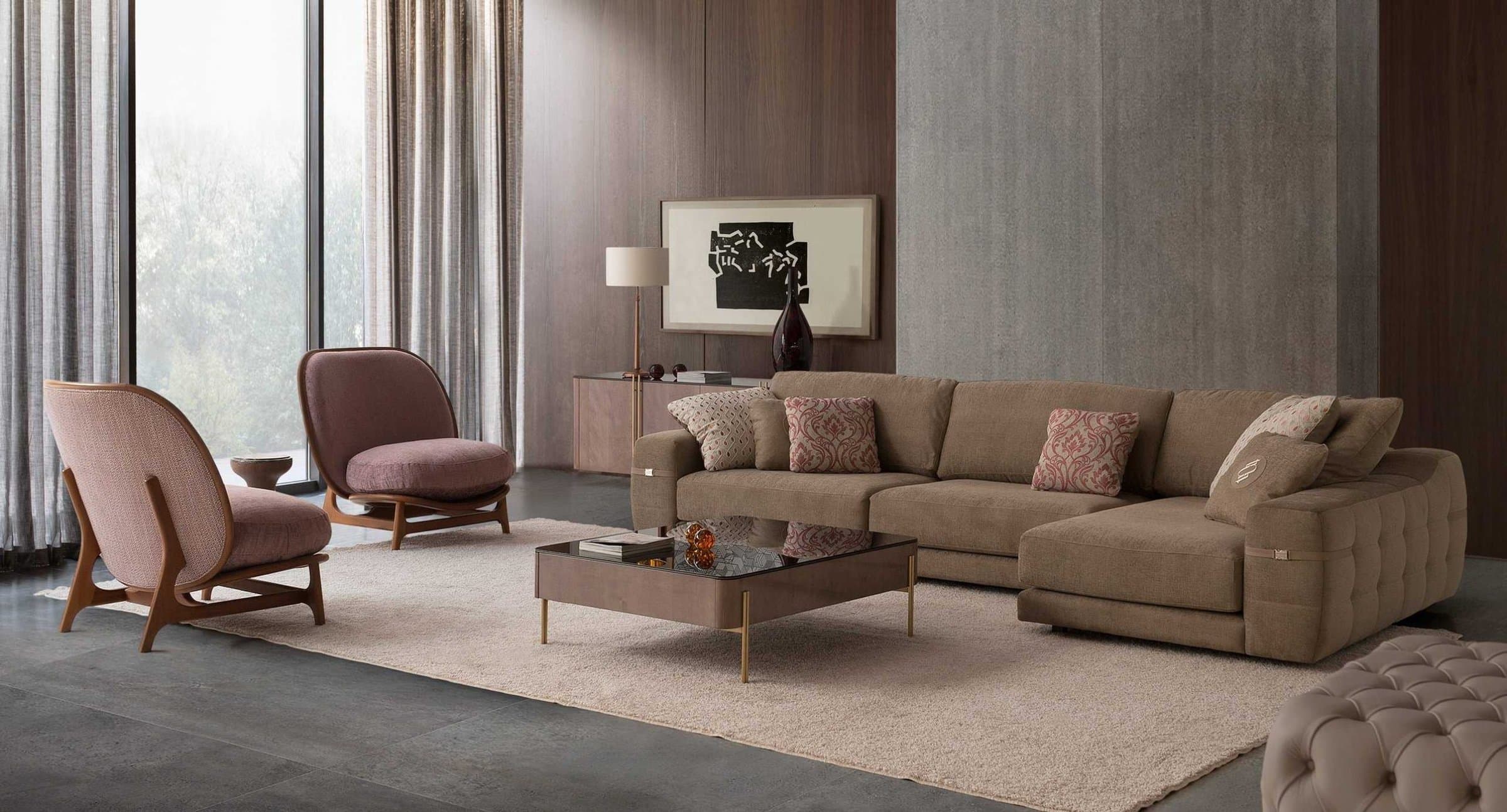 Sofá modular chaise longue en marrón con cojines estampados junto a dos butacas rosas y mesa de centro de cristal