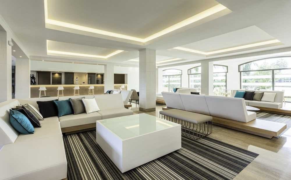 Sala de estar de hotel con sofás blancos modulares, mesa de centro y suelo de madera junto a ventanales