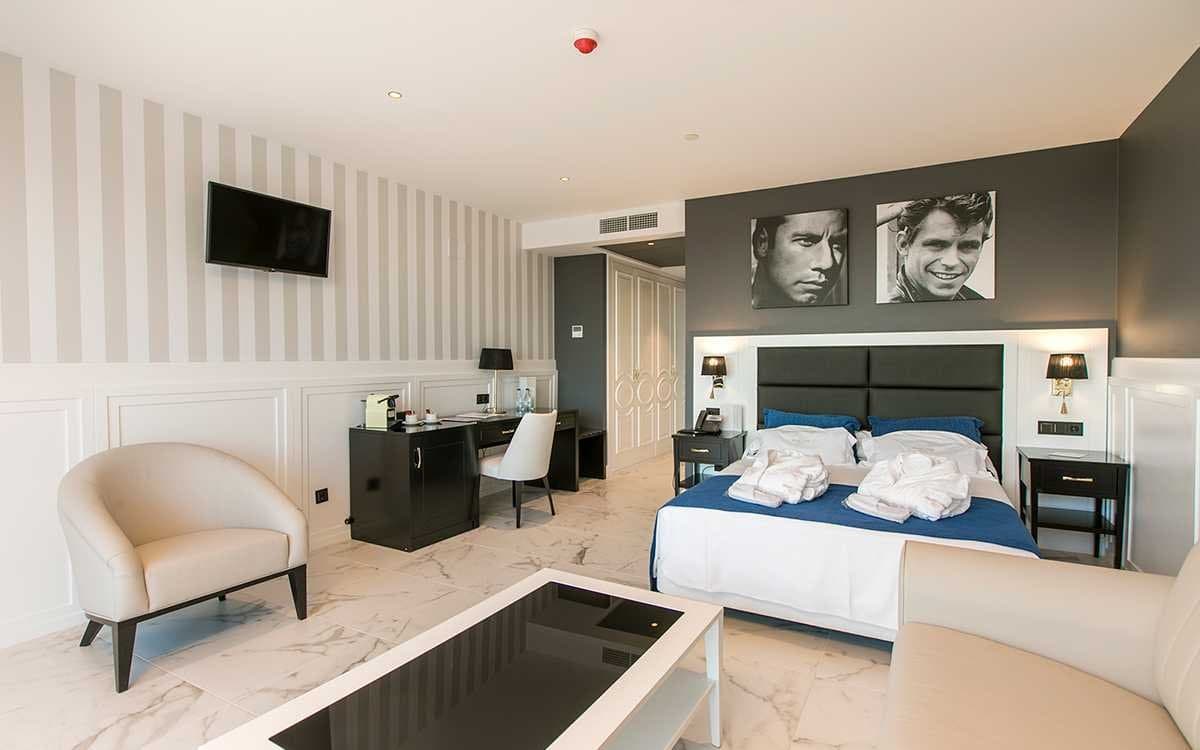 Dormitorio de hotel con retratos en blanco y negro sobre la cabecera oscura y toallas blancas sobre la cama