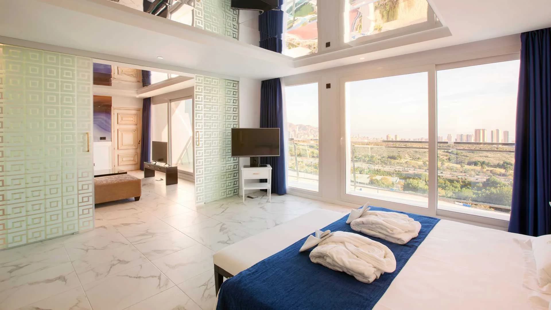 Habitación de hotel con toallas dobladas en forma de cisne, vistas panorámicas a la ciudad y altillo con espejo