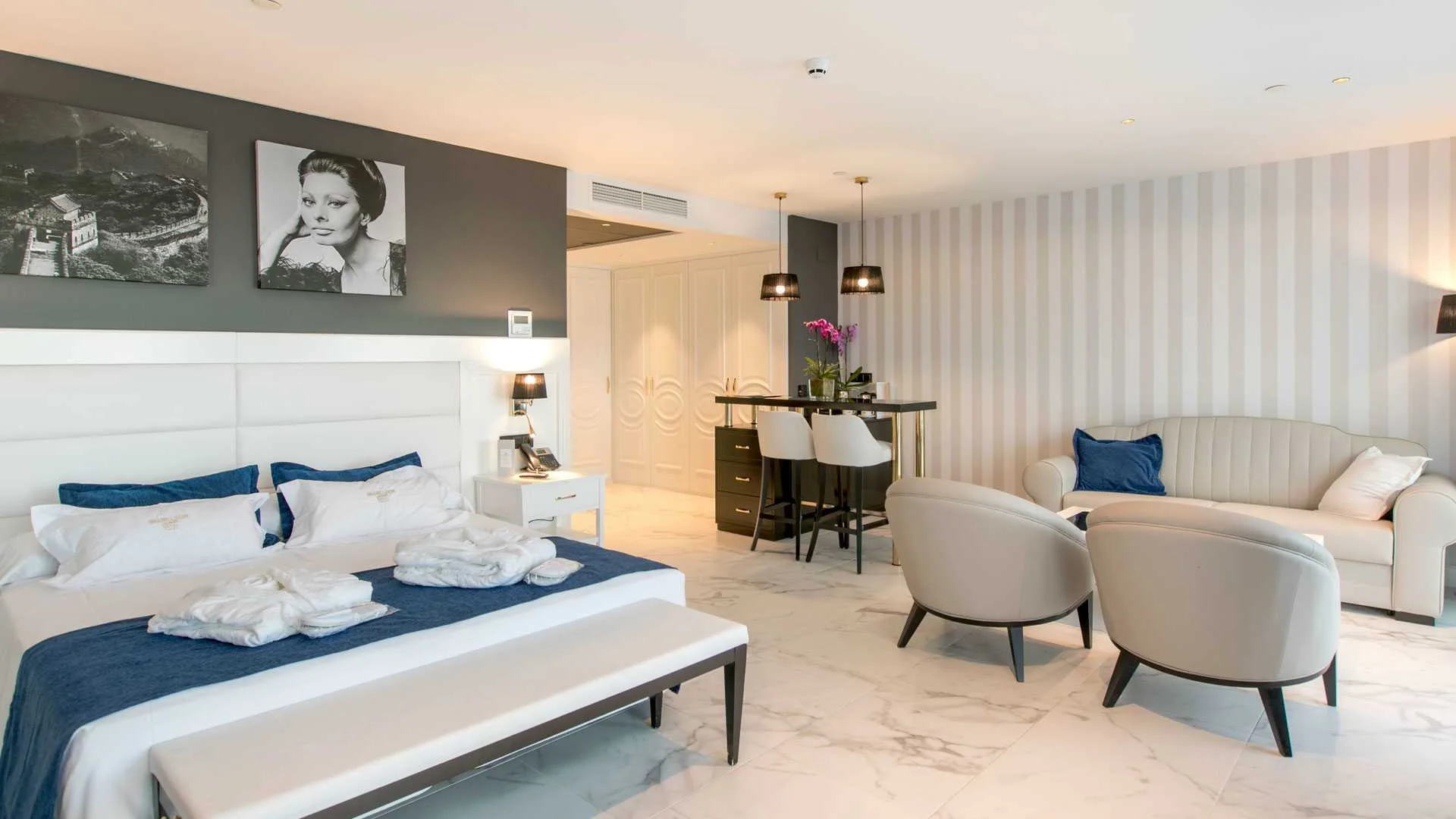 Dormitorio de hotel con retratos en blanco y negro de estilo clásico sobre la cabecera y papel pintado a rayas