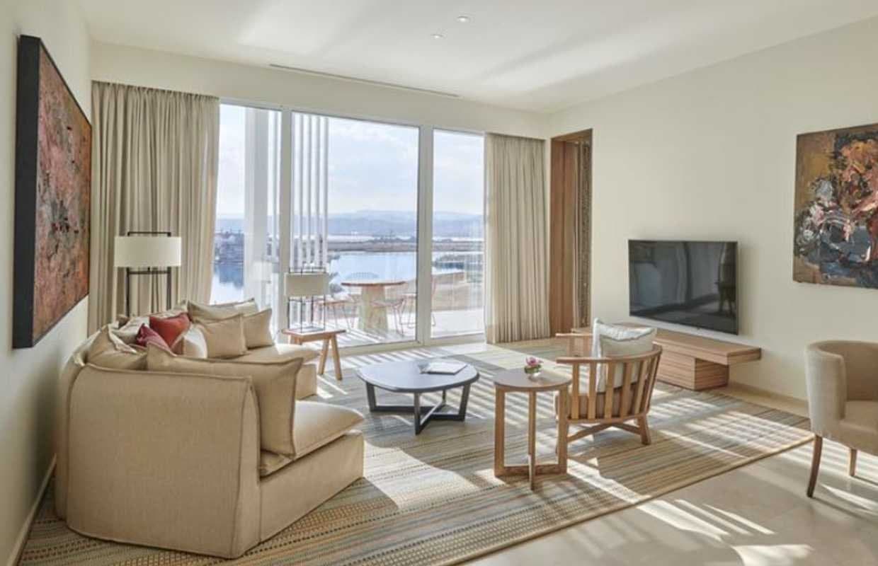 Salón de suite con sofás beige, obras de arte abstracto y vistas a la bahía desde la terraza