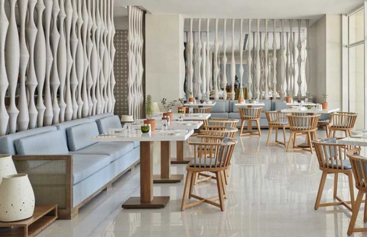 Restaurante de hotel con sofás azul claro, sillas de madera y columnas onduladas decorativas