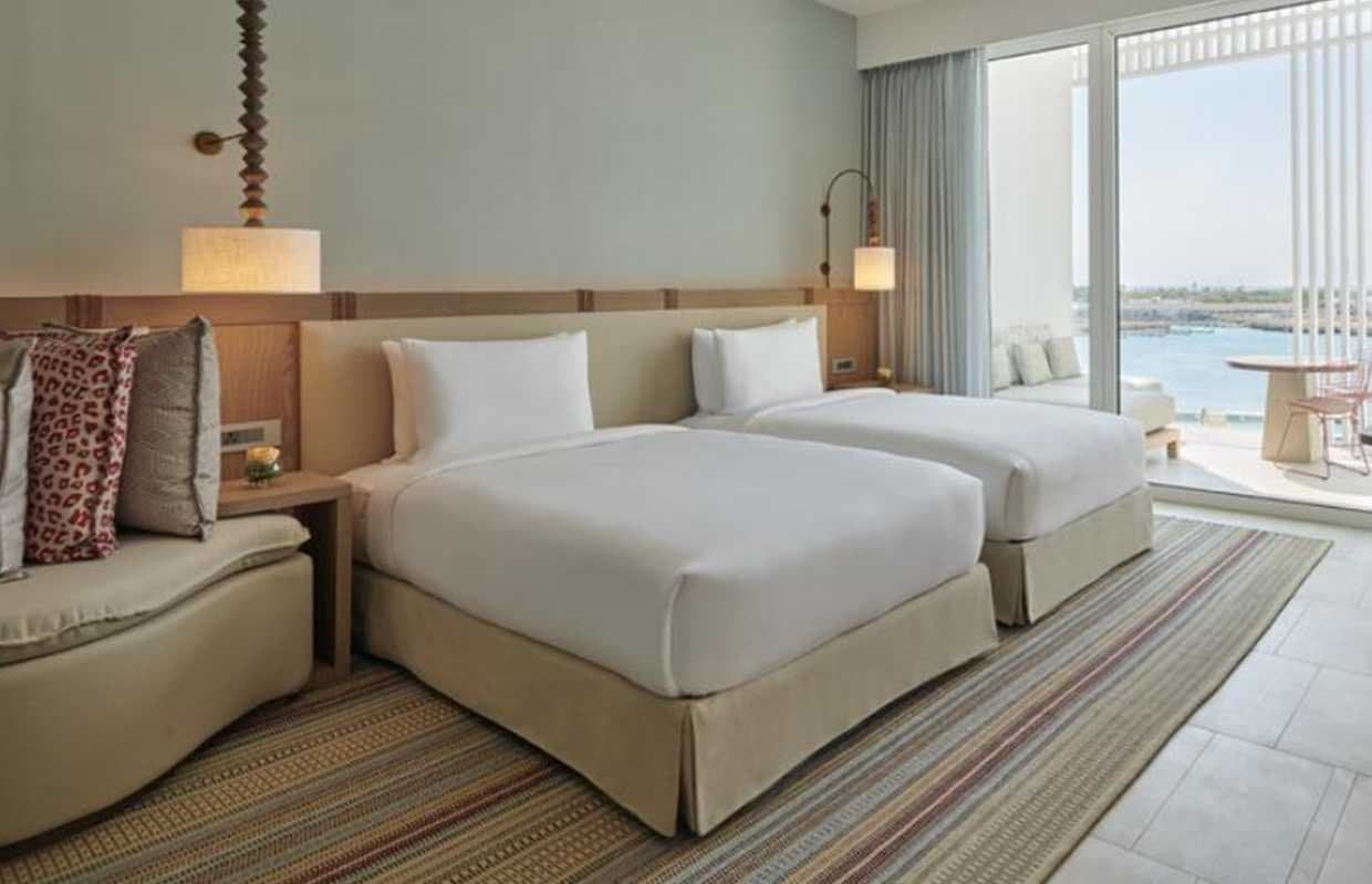 Habitación de hotel con dos camas individuales, lámparas de pared y vistas al mar desde la terraza
