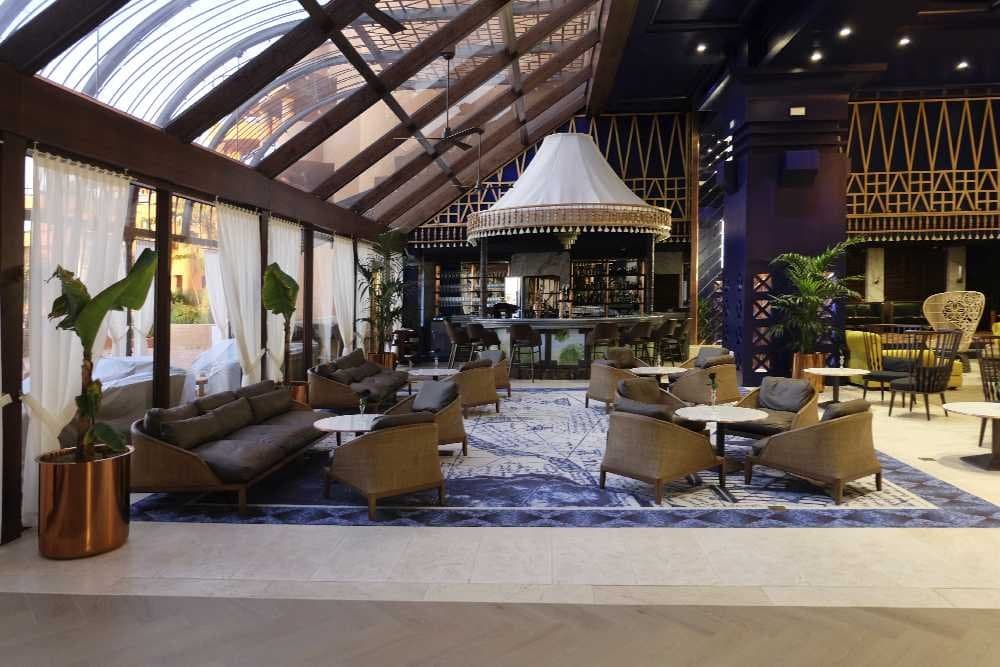 Lobby bar acristalado con techo abovedado, sofás y butacas de mimbre sobre alfombra oscura