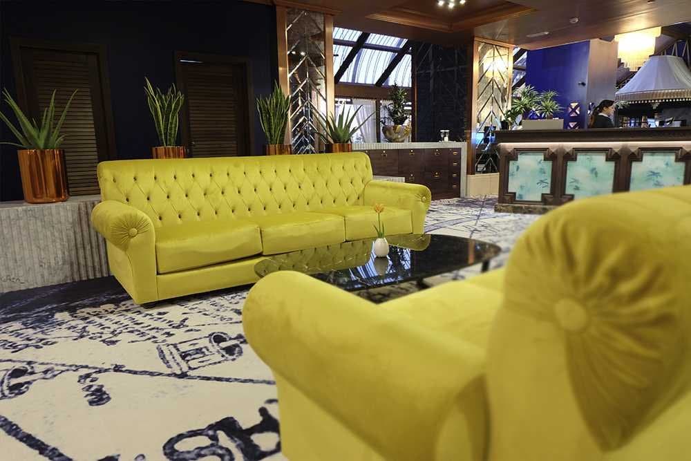Sofá y butaca de terciopelo amarillo capitoné junto a un mostrador de recepción con detalles en madera oscura