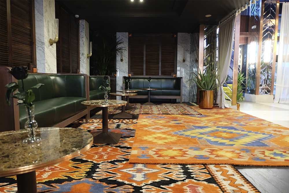 Zona de estar con sofás de piel verde oscuro y alfombras de motivos geométricos en tonos naranja y azul