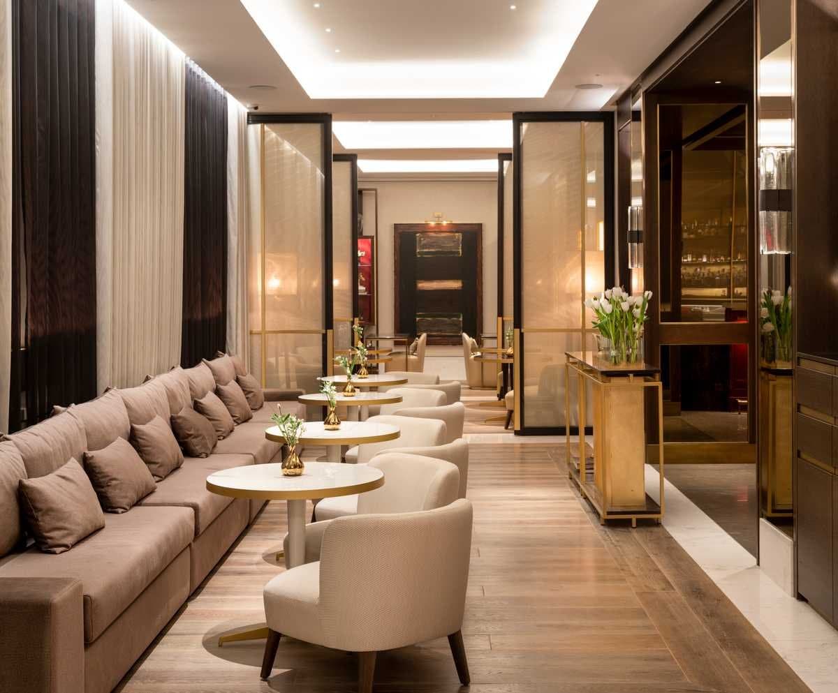 Zona de estar del restaurante con sofá corrido, mesas auxiliares doradas y mamparas de cristal esmerilado