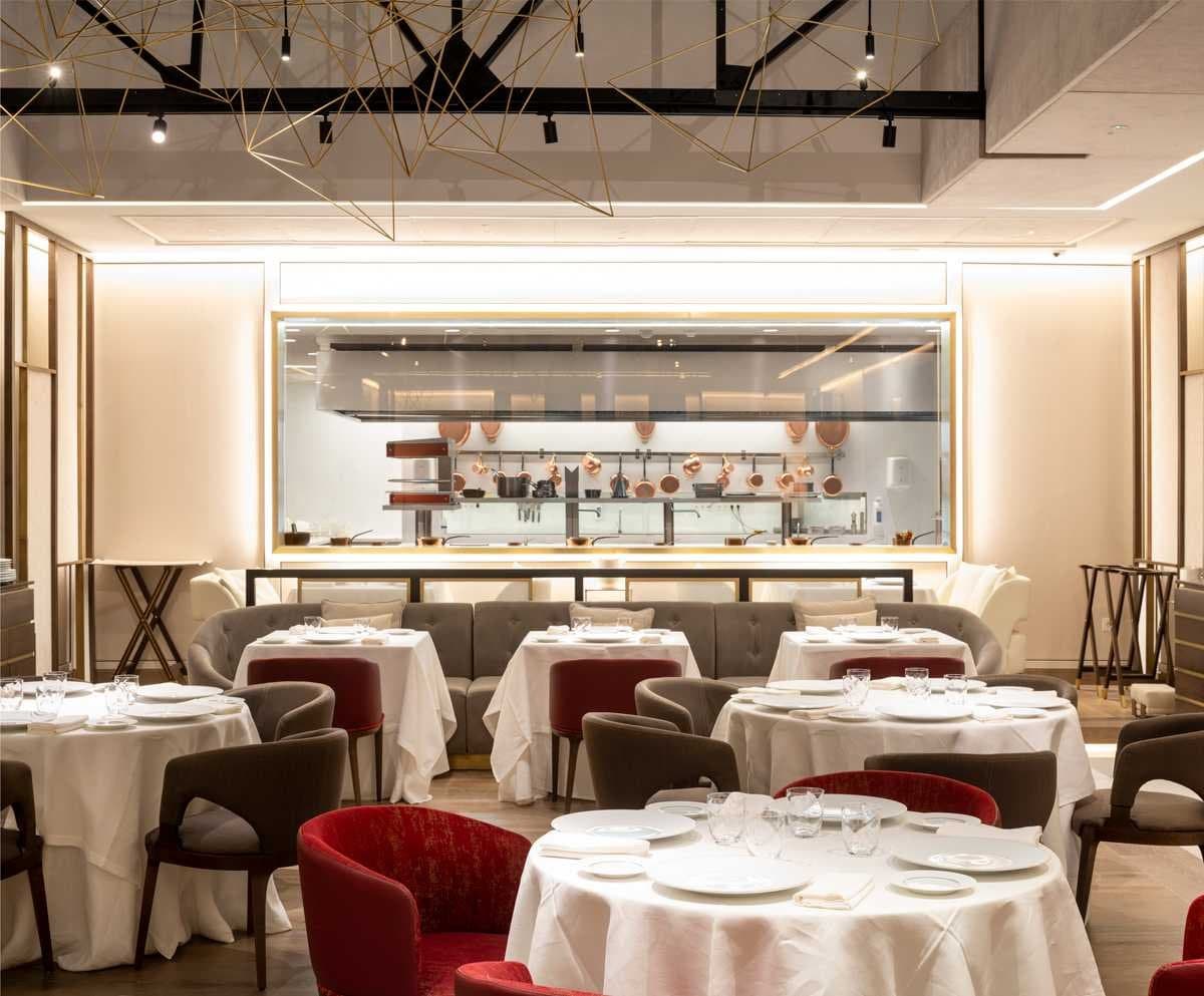 Sala principal del restaurante con escultura lumínica de alambre dorado sobre las mesas y cocina acristalada al fondo
