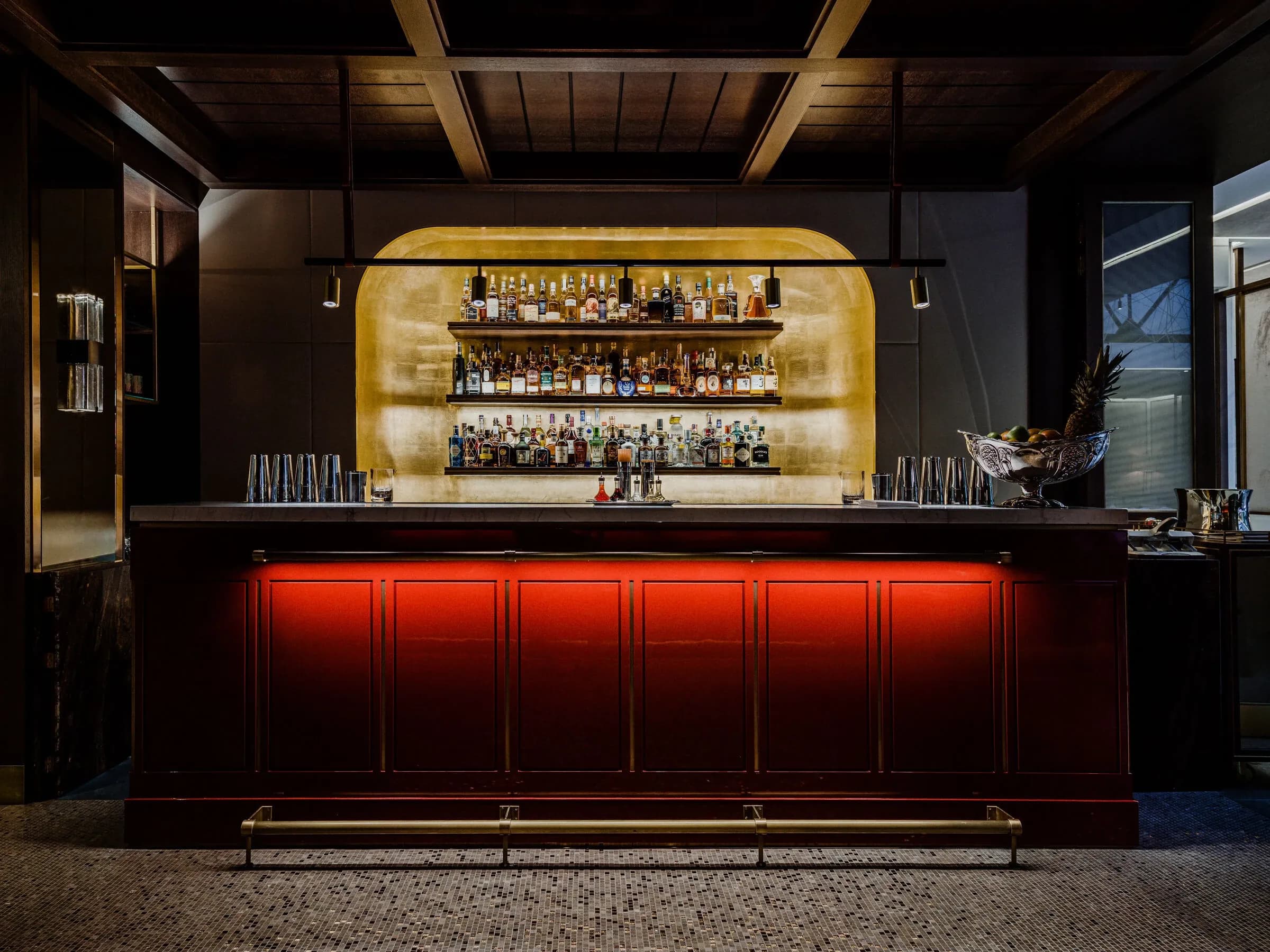 Barra de bar lacada en rojo con iluminación dorada y estantería de licores retroiluminada