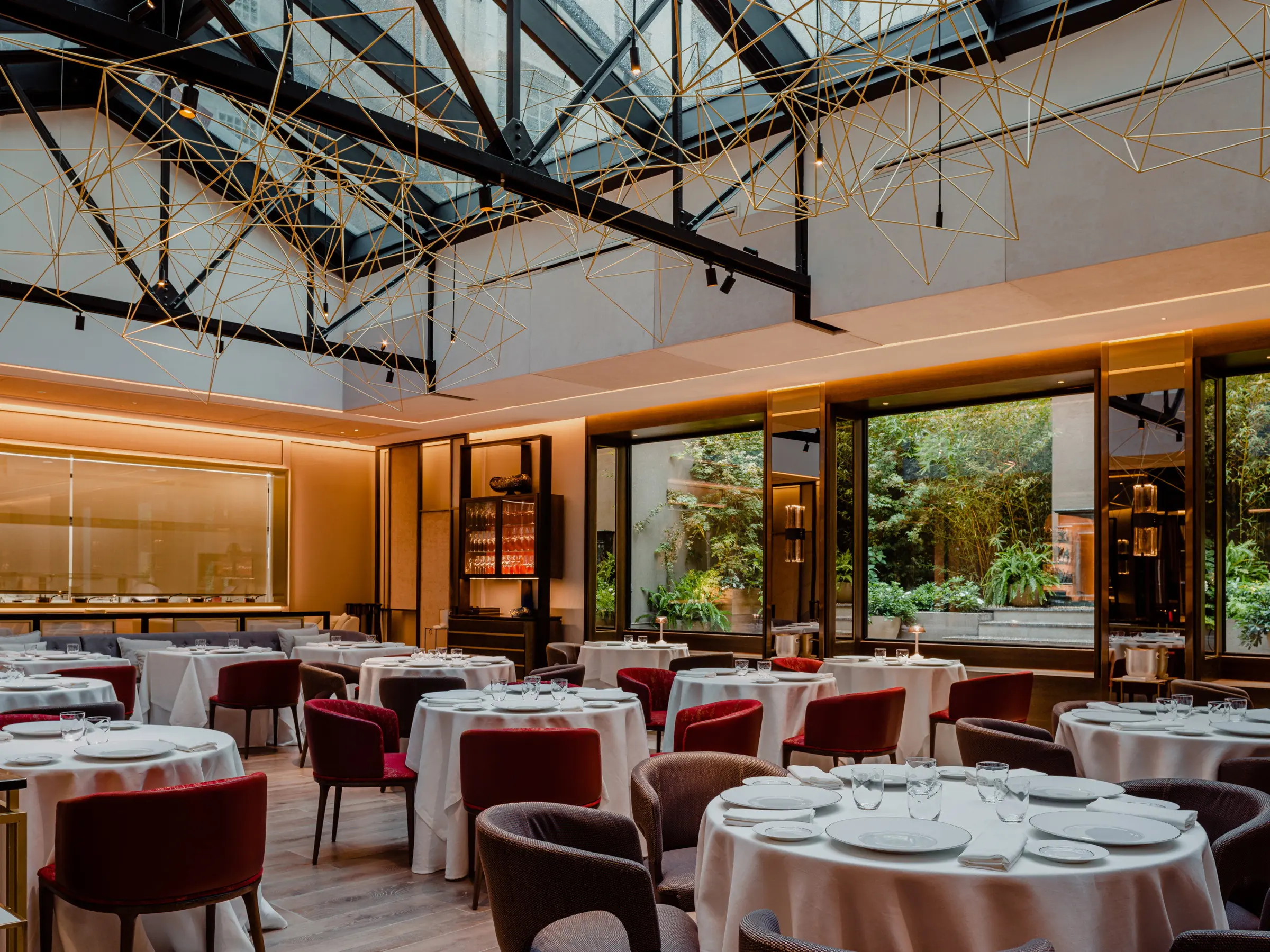 Sala del restaurante con techo acristalado, instalación de luces en forma de constelación y mesas con sillas rojas y grises