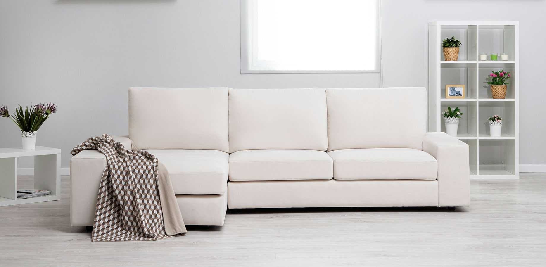 Sofá chaise longue tapizado en color crudo con manta geométrica en un salón con estanterías blancas