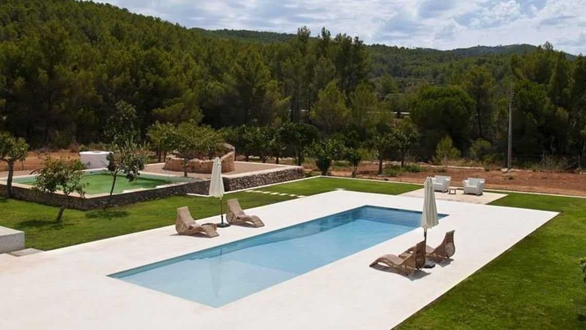 Vista aérea de una piscina rectangular de pavimento de piedra con tumbonas y una piscina infantil junto a un jardín