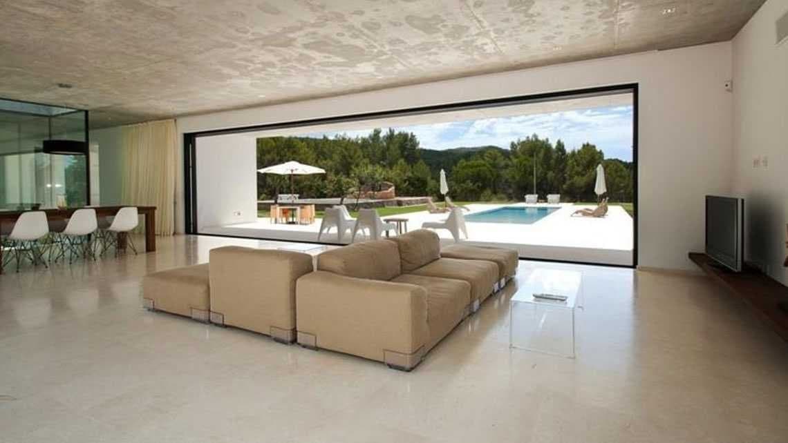 Salón con sofá modular beige frente a un gran ventanal corredizo con vistas a la piscina y la zona ajardinada